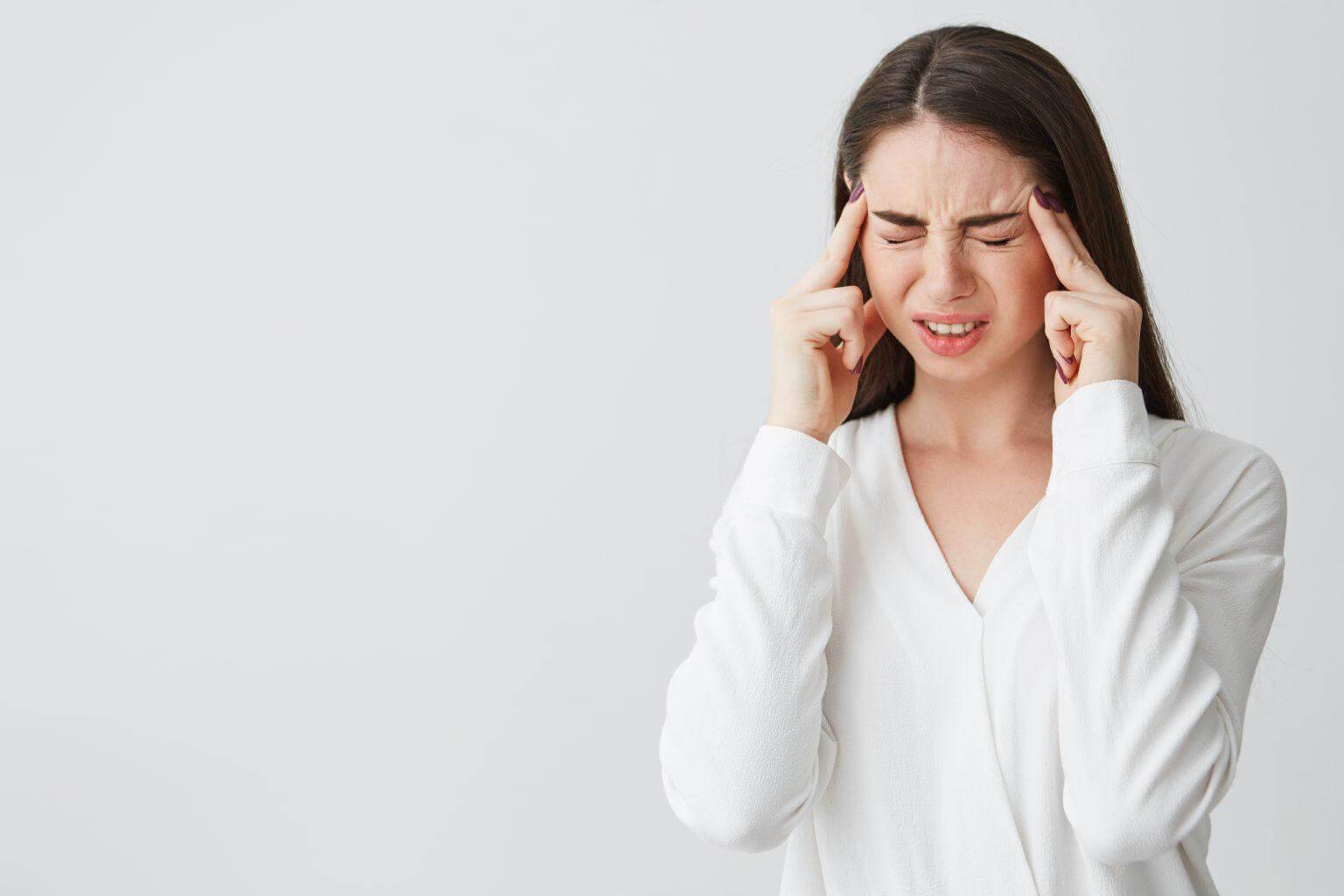 Young beautiful brunette businesswoman holding fingers on temples frowning from pain over white background. Headache.