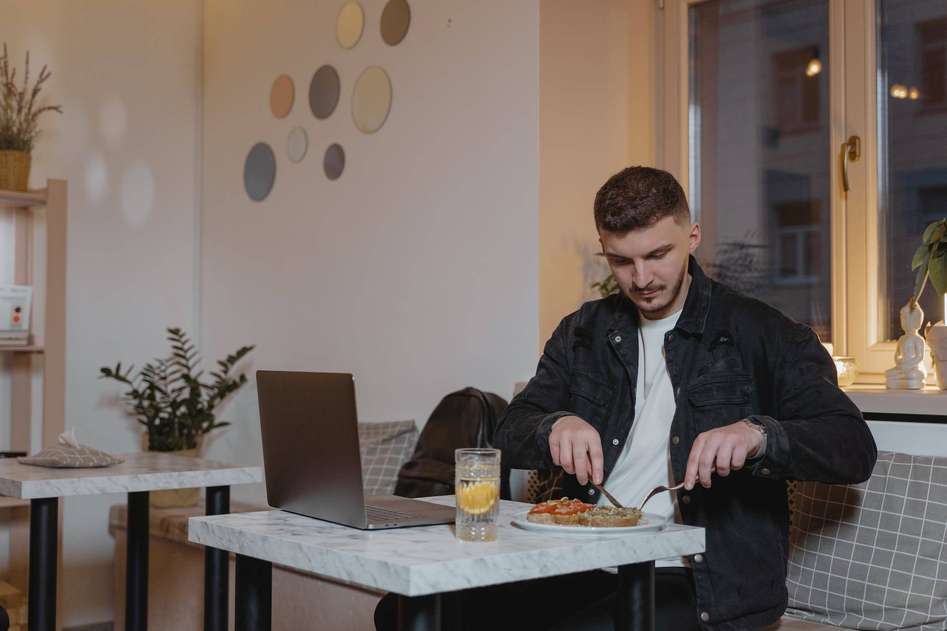 a man in black jacket slicing his food while sitting on the table